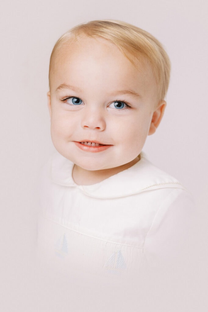 Little 2 year old boy posing for an heirloom portrait in a white peter pan collar outfit with blue sailboats